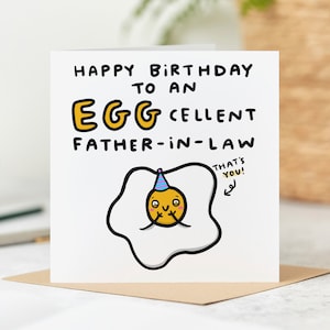 May include: A white card with a black outline of a fried egg with a smiling face wearing a party hat. The text on the card reads "Happy Birthday to an Eggcellent Father-in-Law. That's You!"