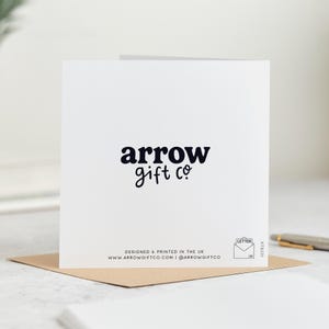 May include: A white greeting card with the text "arrow gift co" in a dark blue font. The card is on a brown envelope. The bottom of the card has the text "DESIGNED & PRINTED IN THE UK" and website and social media information.