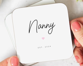May include: White coaster with black text that reads "Nanny" and a small pink heart. The text "EST. 2024" is below the heart.