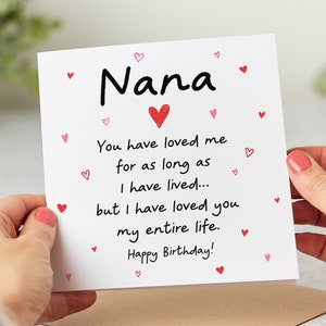 May include: A white card with a red heart and the text "Nana" in black. The card has a message that reads "You have loved me for as long as I have lived... but I have loved you my entire life. Happy Birthday!" with pink hearts scattered around the text.