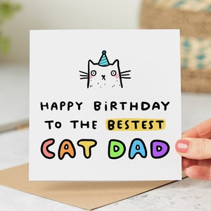 May include: A white card with a cartoon cat wearing a party hat. The card says "Happy Birthday to the Bestest Cat Dad" in colorful letters.