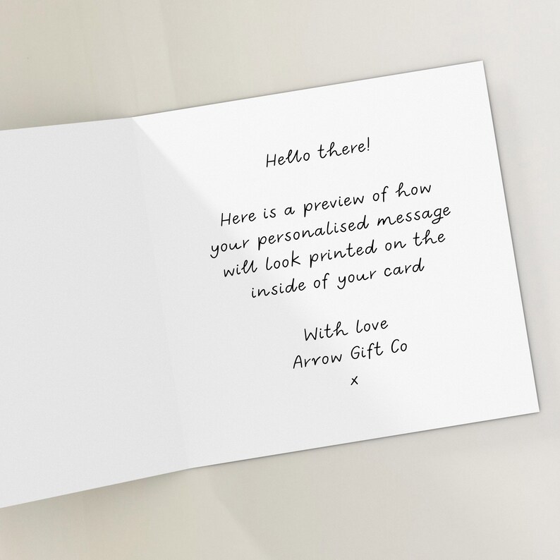 May include: A white card with black text that reads "Hello there! Here is a preview of how your personalised message will look printed on the inside of your card With Love Arrow Gift Co X".