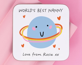 May include: A white square coaster with the text "WORLD'S BEST NANNY" and a blue planet with a smiling face and colorful rings. The text "Love from Rosie xx" is at the bottom of the coaster.