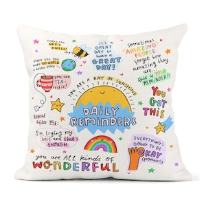 May include: A white cushion with colourful illustrations and text. The text includes "You are a ray of sunshine", "Daily Reminders", "You got this", "Everything's going to be okay (promise!)", "You are all kinds of wonderful", and more.