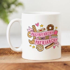 May include: White ceramic mug with a pink and white design featuring a variety of pastries and the text "Pastryarchy not Patriarchy".