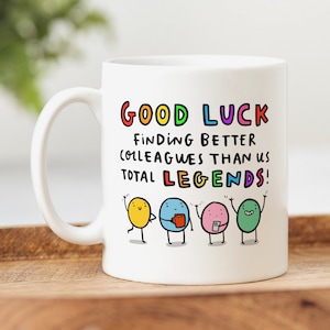 K&ouml;nnte beinhalten: Wei&szlig;e Keramiktasse mit einer bunten Grafik, auf der "Viel Gl&uuml;ck beim Finden von besseren Kollegen als wir, totale Legenden!" steht, mit vier Comicfiguren.