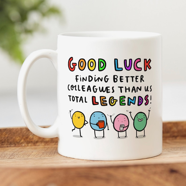 K&ouml;nnte beinhalten: Wei&szlig;e Keramiktasse mit einer bunten Grafik, auf der "Viel Gl&uuml;ck beim Finden von besseren Kollegen als wir, totale Legenden!" steht, mit vier Comicfiguren.