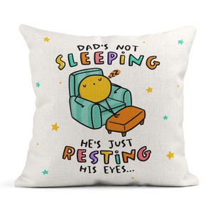 May include: A decorative pillow with the text "DAD'S NOT SLEEPING HE'S JUST RESTING HIS EYES...". The pillow features a cartoon illustration of a yellow figure relaxing in a teal armchair with an orange footstool.