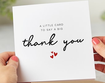 May include: A white card with black text that reads "A little card to say a big thank you". Three small red hearts are below the text.