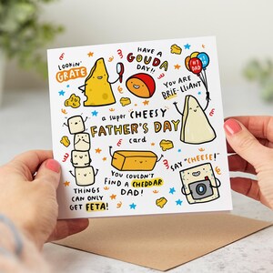 May include: A Father's Day card with a whimsical design featuring cartoon cheese characters. The card includes phrases like "Gouda Day!!" and "You are Brie-lliant." The card is held by a person.