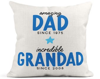May include: White throw pillow with blue text that reads "amazing DAD since 1975" and "incredible GRANDAD since 2008". A blue star is between the two lines of text.