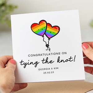 May include: A white card with a rainbow heart balloon design. The card says "Congratulations on tying the knot!" with the names "Georgia & Kim" and the date "25.02.23" printed below.
