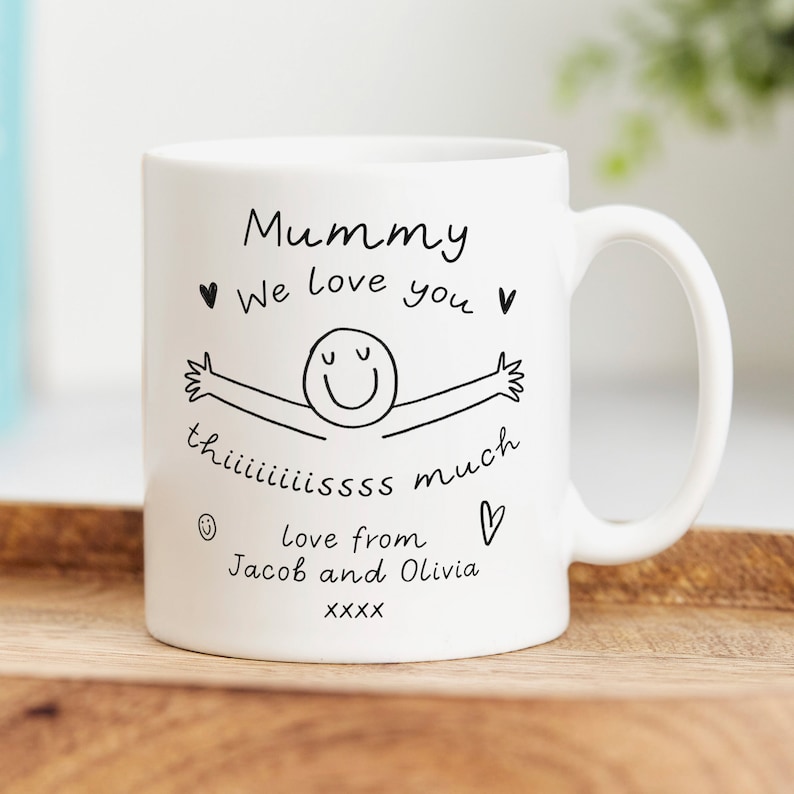 May include: White ceramic mug with a black hand-drawn illustration of a smiling person with outstretched arms. The text reads "Mummy &hearts; We love you &hearts; th iiiiiissss much  love from Jacob and Olivia XXXX &hearts;".