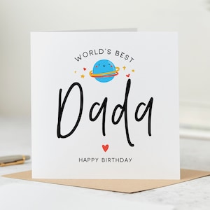 May include: A white card with the text "World's Best Dada Happy Birthday" in black. A blue planet with a happy face and red hearts is above the text.
