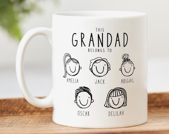 May include: White ceramic mug with the text "THIS GRANDAD BELONGS TO" and six cartoon faces with names: Amelia, Jack, Abigail, Oscar, and Delilah. The mug has a curved handle and is on a wooden surface.