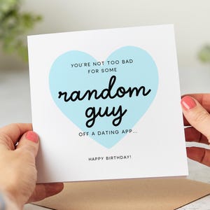 May include: A light blue heart with the text "YOU'RE NOT TOO BAD FOR SOME random guy OFF A DATING APP... HAPPY BIRTHDAY!" on a white card.