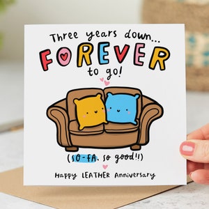 May include: A white card with a colourful illustration of a sofa with two cushions. The text on the card reads "Three years down...FOREVER to go! (SO-FA. so good!!) Happy LEATHER Anniversary."