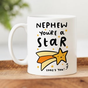 May include: White ceramic mug with a black and yellow design. The mug says "Nephew you're a star that's you!" with a cartoon shooting star.