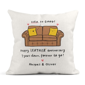 May include: A white cushion featuring a brown sofa illustration and the text "SOFA, SO GOOD!". The cushion also includes the text "Happy LEATHER anniversary 3 years down, forever to go! Abigail & Oliver".