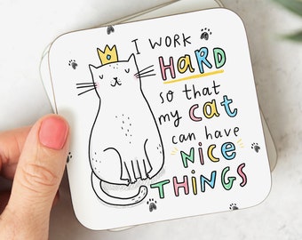 May include: White coaster with a cartoon cat wearing a crown. The text reads "I work hard so that my cat can have nice things".