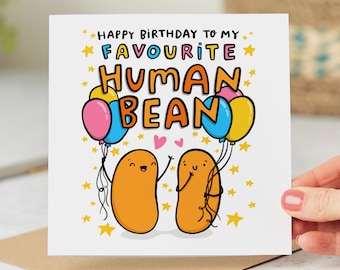 May include: A white card with a birthday message that says "Happy Birthday to my favorite human bean." The card features two cartoon beans holding hands with hearts above them. The beans are orange and have happy faces. There are yellow stars and colorful balloons around the beans.