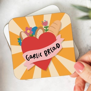 May include: A yellow and white striped background with a red heart in the centre. The heart has a pink ribbon wrapped around it with the text "Garlic Bread". The heart is surrounded by flowers and a loaf of bread.