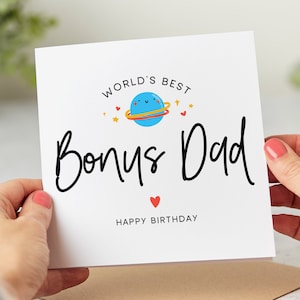 May include: A white card with black text that reads "World's Best Bonus Dad Happy Birthday". A blue planet with a happy face and a red heart is illustrated above the text.