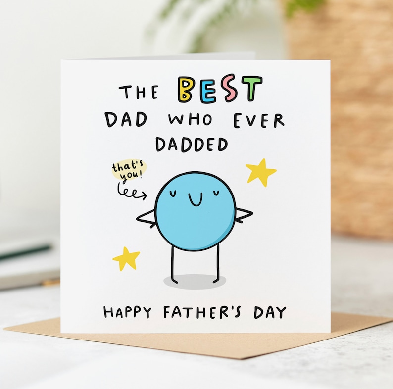 May include: A white card with a blue cartoon character with a happy face and the text "The Best Dad Who Ever Dadded" and "Happy Father's Day".