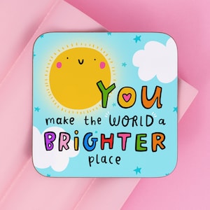 May include: A blue and white coaster with a yellow sun, white clouds, and stars. The text "You make the world a brighter place" is written in colourful letters.