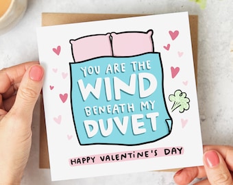 May include: A Valentine's Day card with a humorous design. The card features a cartoon illustration of a bed with pillows and a duvet, with the text "You are the wind beneath my duvet." Pink hearts and the words "Happy Valentine's Day" are also included.