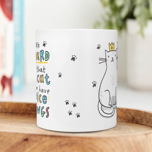 May include: White ceramic mug with a black and white illustration of a cat wearing a gold crown. The text on the mug reads "Work hard that cat can have nice things".