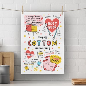 May include: A white kitchen towel with a colourful illustration of a cotton anniversary theme. The illustration includes a couple of spools of thread, a pair of socks, and a heart with the text "Best Buds". The text "Happy Cotton Anniversary" is written in large, colourful letters. The date "25.02.21" is written in the bottom left corner. The text "I'm Sew into You" is written in the centre of the towel.