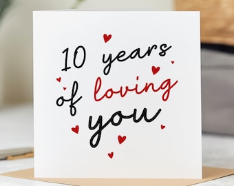 Puede incluir: Tarjeta blanca con corazones rojos y texto negro que dice "10 años de amarte".