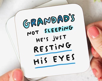 May include: White square coaster with blue and black text that reads "Grandad's not sleeping he's just resting his eyes".