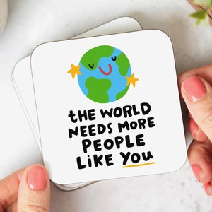 May include: White coaster with a cartoon illustration of a smiling earth with stars. The text reads "The world needs more people like you."