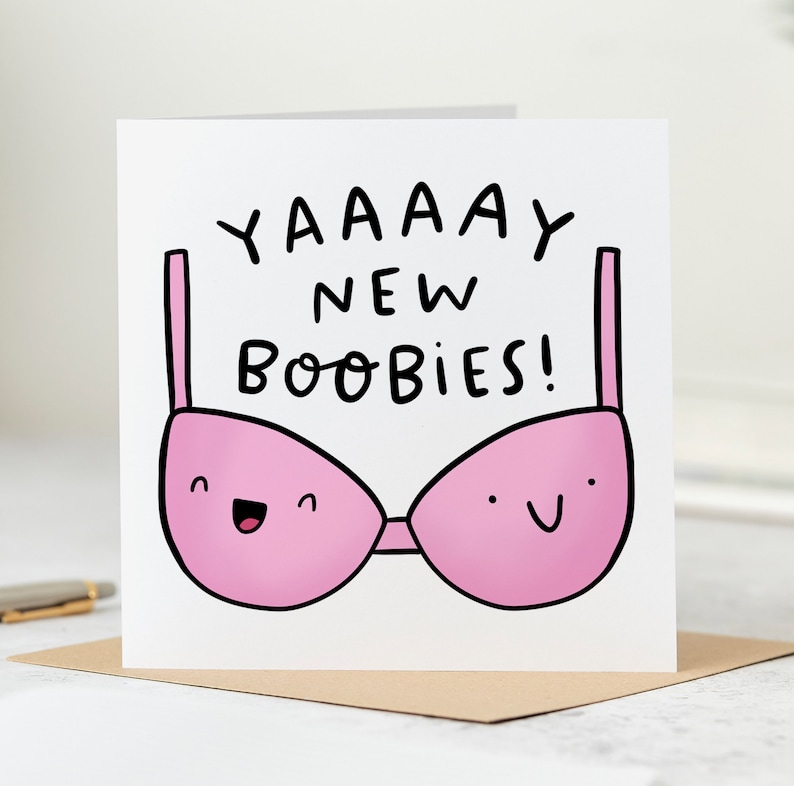May include: A white card with black text that reads "YAAAAAY NEW BOOBIES!" and a pink bra with a smiling face on each cup.