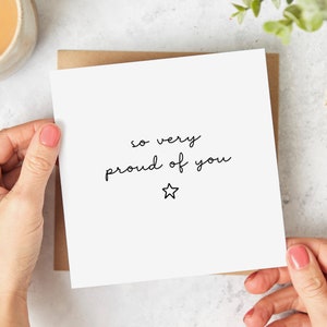 May include: A white card with black text that reads "so very proud of you" and a small black star.