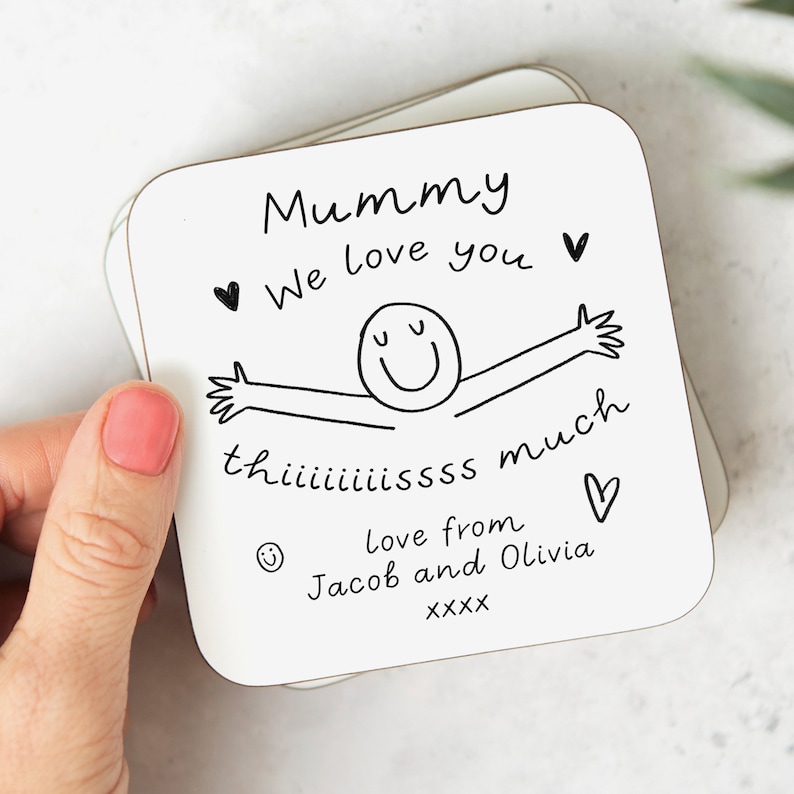 May include: White square coaster with black text and a simple drawing of a person with arms outstretched. The text reads "Mummy We love you" with a heart symbol, "thiiiiiiiissss much" with a heart symbol, "Love from Jacob and Olivia" with a smiley face symbol, and "XXXX".