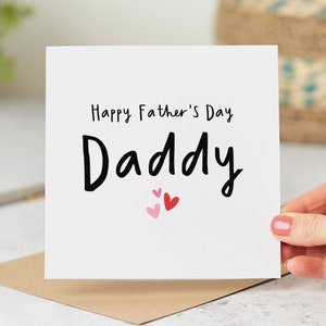 May include: White card with black text that reads "Happy Father's Day Daddy" with three pink and red hearts.