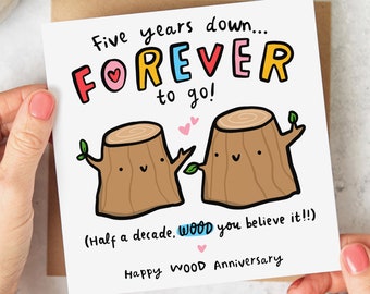 May include: A greeting card with a cartoon illustration of two tree stumps holding hands. The card says "Five years down...FOREVER to go! (Half a decade, WOOD you believe it!!) Happy WOOD Anniversary".