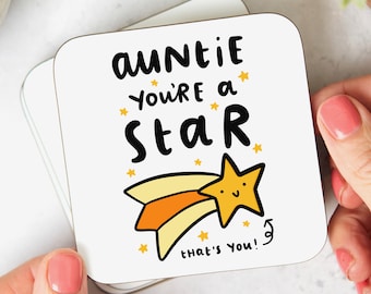 May include: White coaster with the text "Auntie you're a star that's you!" in black. A yellow star with a smiling face is drawn next to the text. The star is on a yellow and orange shooting star.