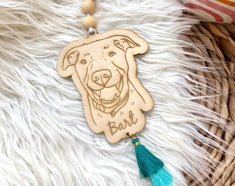May include: Wooden car air freshener with a dog's face and the name "Bart" engraved on it. The air freshener has a teal, blue, and white tassel.