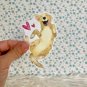 May include: A sticker of a cartoon golden retriever dog with its tongue sticking out and two pink hearts above it. The dog is on a white background.