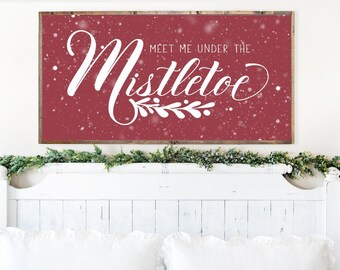 May include: A red wooden sign with white snow-like flecks and the text "Meet me under the mistletoe" in white cursive lettering.