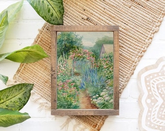 May include: A framed watercolor painting depicting a garden path leading to a small house. The path is lined with lush greenery and colorful flowers, including pink, blue, and white blooms. The house is painted in a light blue color with a white trim.