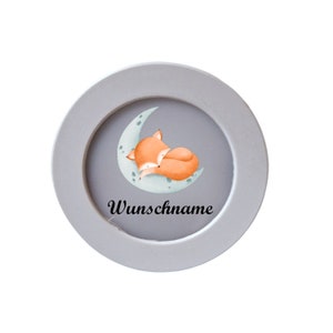 Könnte beinhalten: Ein runder, grauer Bilderrahmen mit einer Aquarellillustration eines schlafenden orangefarbenen Fuchses auf einem Mond. Der Hintergrund ist grau, und der Text "Wunschname" ist in Schwarz geschrieben.