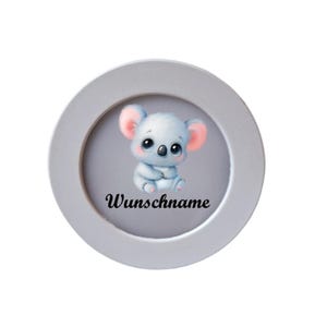 Könnte beinhalten: Ein rundes, weiß gerahmtes Bild mit einem niedlichen Cartoon-Koala-Bären mit großen Augen und rosa Ohren. Der Koala sitzt auf grauem Hintergrund, darunter steht in schwarzer Schrift das Wort "Wunschname".
