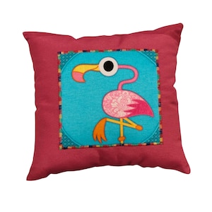 Könnte beinhalten: Ein quadratisches Zierkissen mit einem Flamingomotiv. Das Kissen hat einen magentafarbenen Rand und eine türkisfarbene Mitte mit einer rosa Flamingo-Illustration. Der Flamingo hat einen gelben Schnabel und Beine sowie ein weißes Auge.