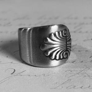 May include: A silver ring with a detailed, stylized floral design. The ring is made from recycled materials and has a rustic, vintage look.