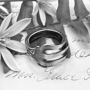 May include: A silver-toned metal ring crafted from a repurposed fork, featuring the distinct tines of the utensil curving around the band. The interior of the ring is clearly stamped with the text 223, visible in this black and white image.